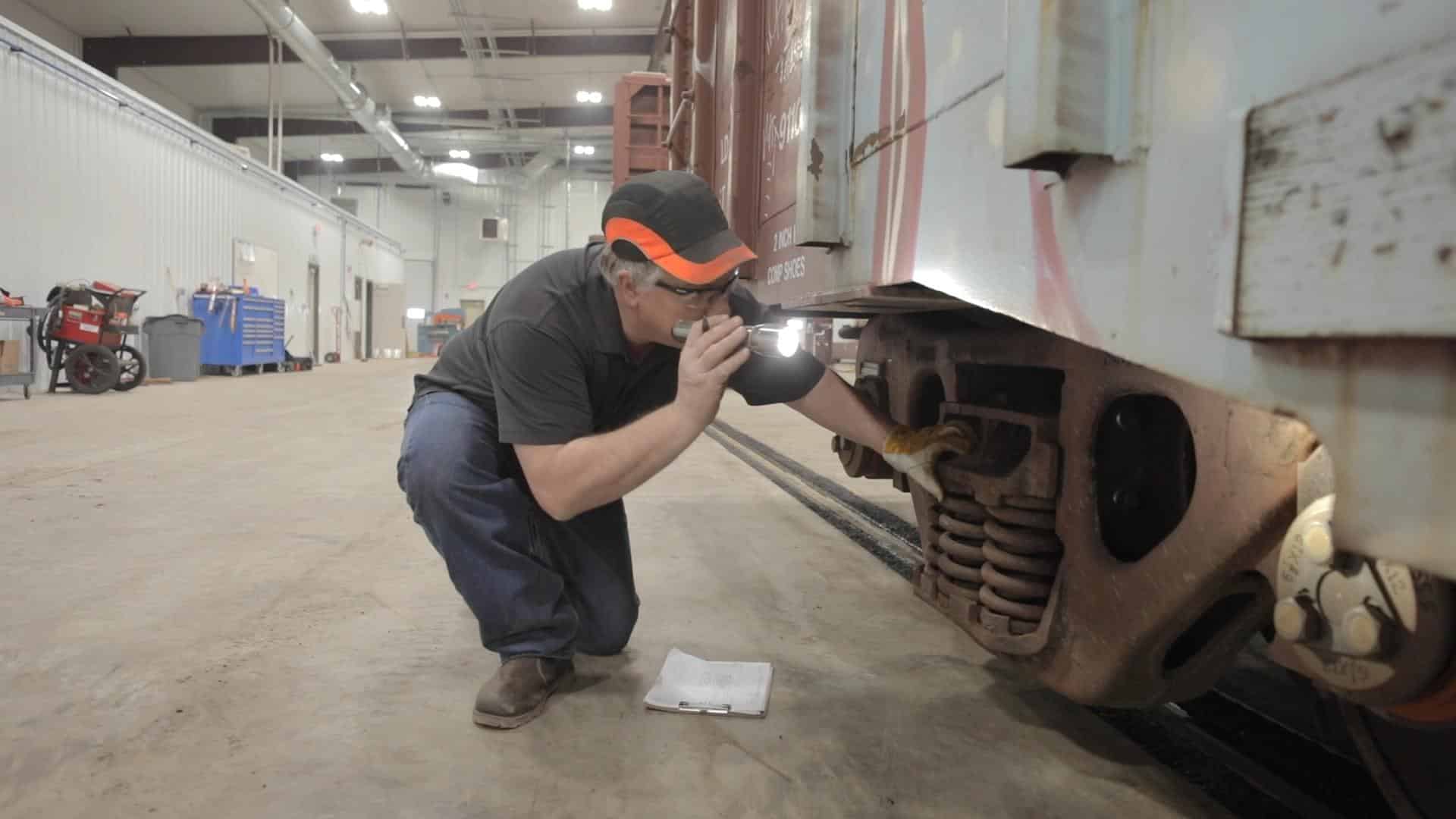 A man crouching down to inspect part of a train car with a flashlight